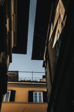 View of a narrow alleyway between old buildings with deep shadows and interesting architectural lines. The sky is visible overhead, lending contrast and depth to the scene.