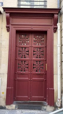 Tarihi bir taş binanın ön cephesine ince detaylar kazınmış kırmızı ahşap kapı. Dekoratif paneller gösterişli, karmaşık işçilik. İşaretler tüm katlarda gaz bulunabileceğini gösteriyor..