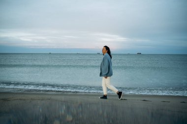 Alacakaranlıkta sakin bir plajda huzur içinde yürüyen kadın, rahatlatıcı dalgaların sesinin tadını çıkarıyor. Huzurlu okyanus arkaplanı rahatlama ve yansıma hissi veriyor. Dizinin bir parçası