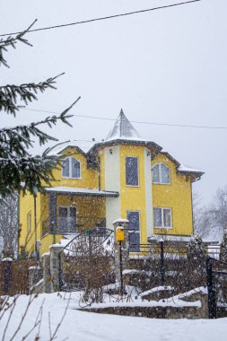 Köydeki kar yağışı sırasında sarı kırsal ev. Sarı ahşap ev, orman arka planında, yoğun kar altında. Skhidnytsia, Ukrayna