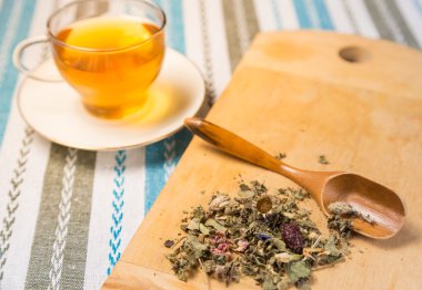 Bir fincan çay bir yığın ahşap bir masa üzerine kuru otlar ile