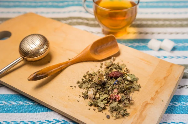 Una tazza di tè con un mucchio di erbe secche su una scrivania di legno — Foto Stock