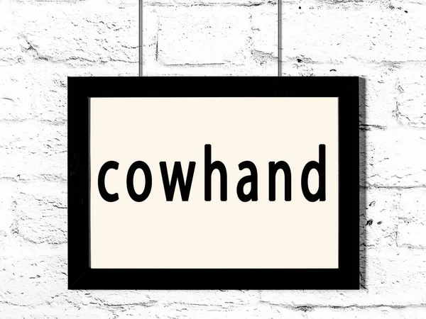 Μαύρο πλαίσιο κρέμεται σε λευκό τοίχο τούβλο με επιγραφή cowhand — Φωτογραφία Αρχείου