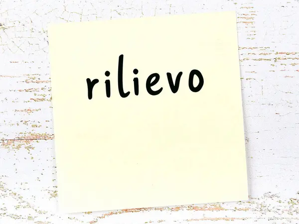 Yellow sticky note on wooden wall with handwritten word rilievo — Stock Photo, Image