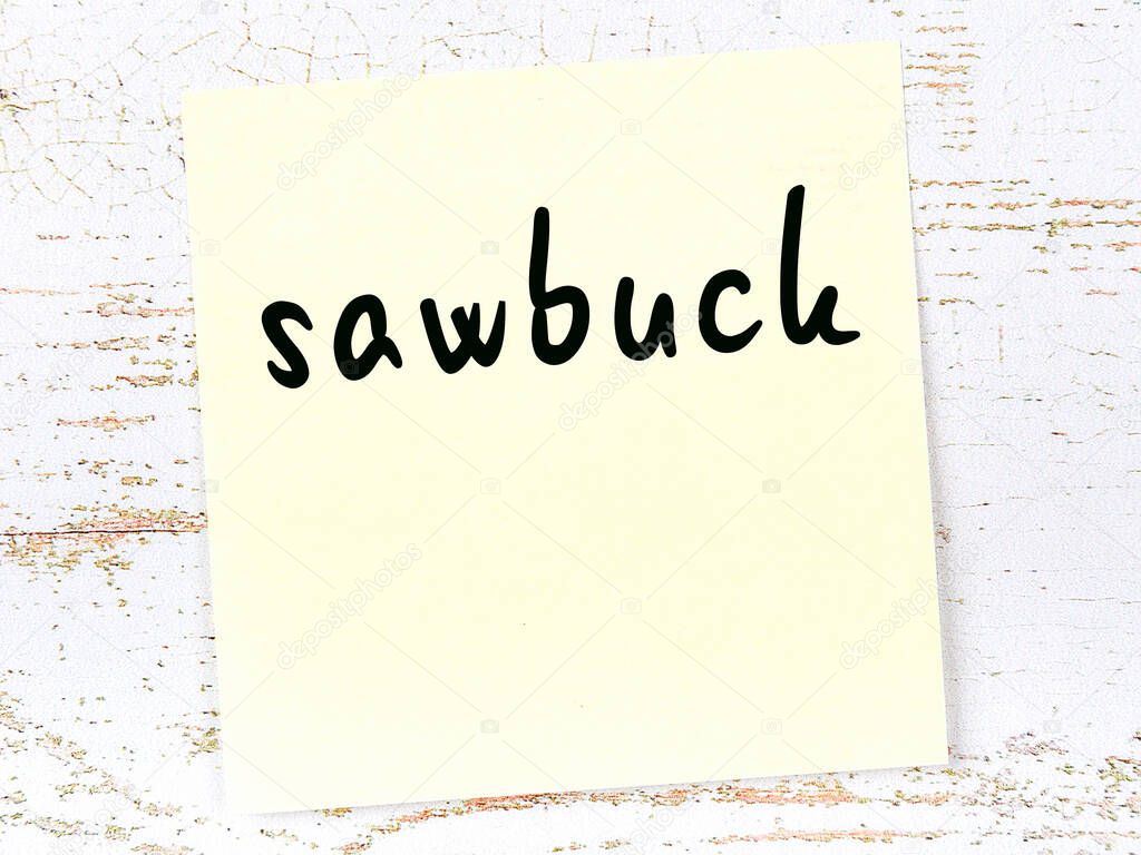Yellow sticky note on wooden wall with handwritten word sawbuck