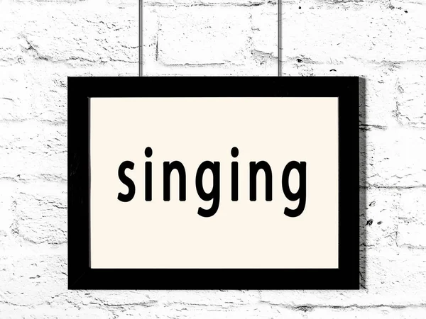 Czarna ramka wisząca na białej ceglanej ścianie z napisem śpiew — Zdjęcie stockowe