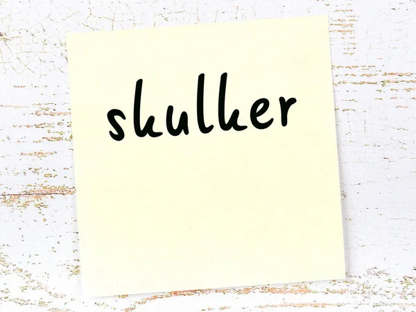Κίτρινο φύλλο χαρτί με λέξη skulker. Έννοια υπενθύμισης — Φωτογραφία Αρχείου