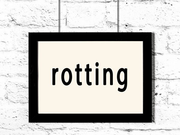 Black frame hanging on white brick wall with inscription rotting