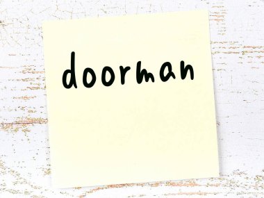 Tahta duvarda sarı yapışkan bir not ve el yazısıyla yazılmış bir kapıcı.