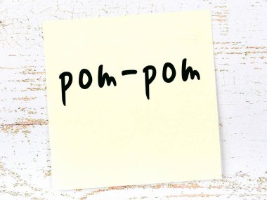 Tahta duvardaki sarı yapışkan notta el yazısı pom-pon yazıyor.