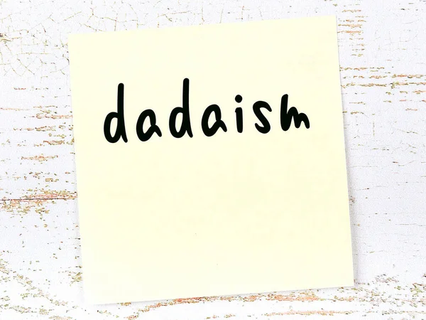Żółta, lepka nuta na drewnianej ścianie z ręcznie napisanym słowem dadaism — Zdjęcie stockowe