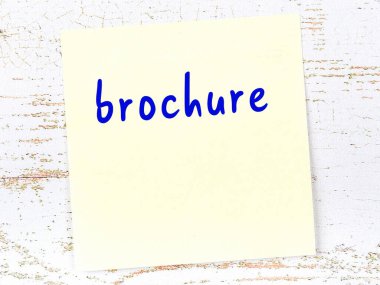 Tahta duvarda el yazısıyla yazılmış broşürlü sarı yapışkan bir not var.