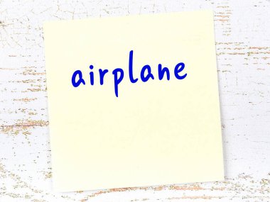 Tahta duvardaki sarı yapışkan notta el yazısıyla yazılmış uçak.