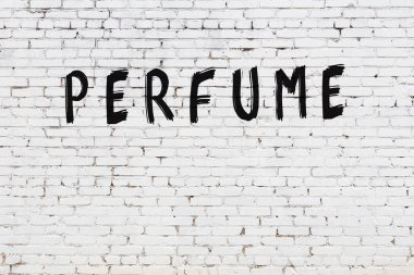 Üzerinde siyah boya ile el yazısıyla parfüm yazan beyaz tuğla bir duvar.