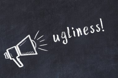 Hoparlörün tebeşir çizimi ve siyah masanın üzerine el yazısıyla yazılmış çirkinlik.