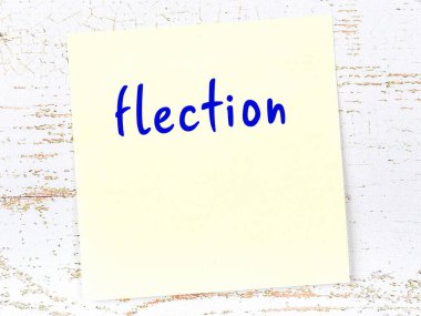 Tahta duvarda el yazısıyla yazılmış sarı yapışkan bir not var.