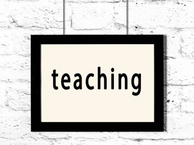 Üzerinde yazı olan siyah ahşap çerçeve beyaz tuğla duvarda asılı duruyor. 