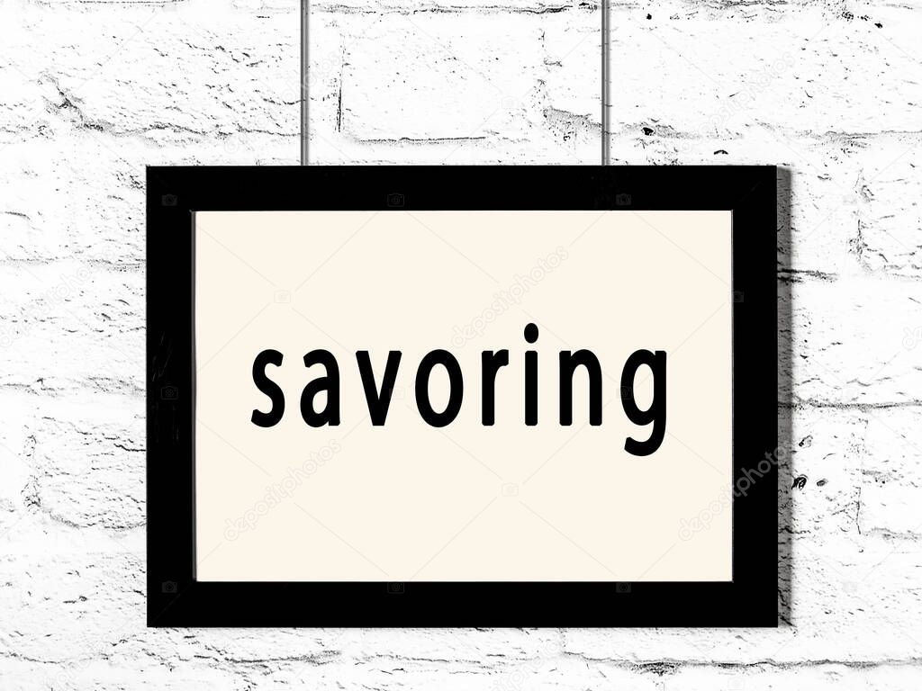 Black wooden frame with inscription savoring hanging on white brick wall 