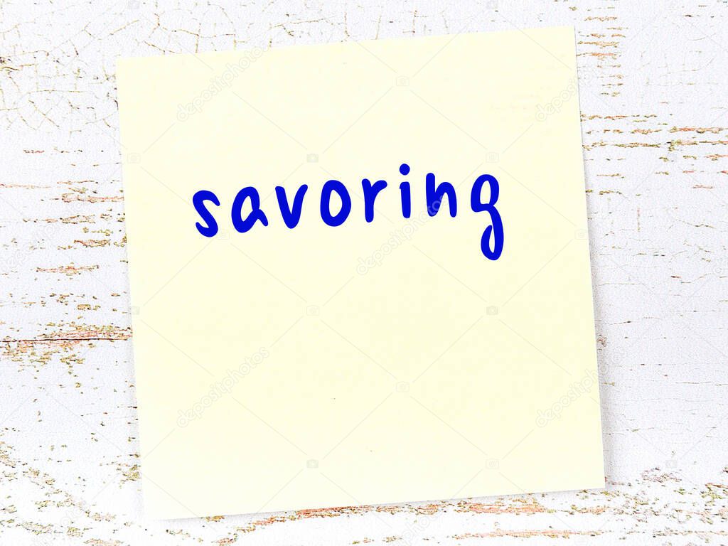 Concept of reminder about savoring. Yellow sticky sheet of paper on wooden wall with inscription
