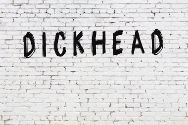 Inscription dickhead written with black paint on white brick wall.