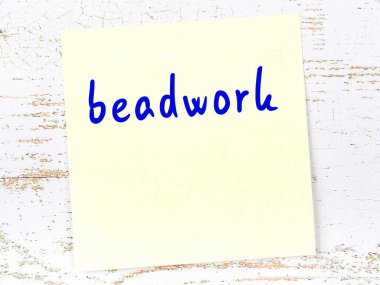 Tahta duvarda el yazısıyla yazılmış boncuk işçiliği olan sarı yapışkan bir not.