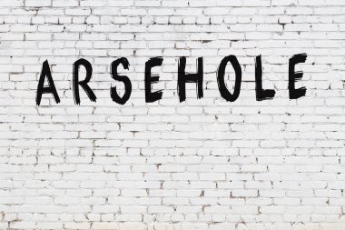 Inscription arsehole written with black paint on white brick wall.