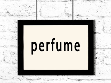 Siyah ahşap çerçeve, beyaz tuğla duvarda yazı parfümü asılı. 