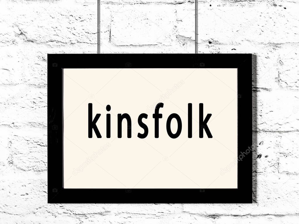 Black wooden frame with inscription kinsfolk hanging on white brick wall 