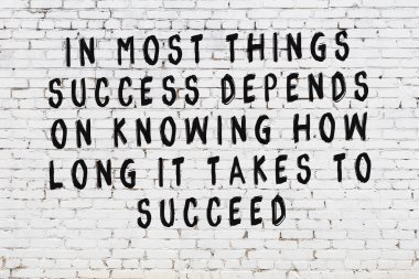 Beyaz tuğla duvara zekice alıntılar yazılı siyah bir yazı.