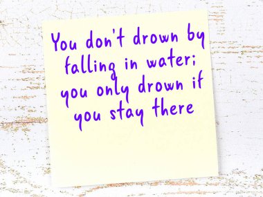 Tahta duvarda asılı sarı yapışkan nota elle yazılmış bilgece bir alıntı.