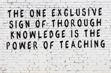 Beyaz tuğla duvara zekice alıntılar yazılı siyah bir yazı.