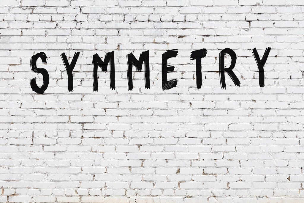 Inscription symmetry written with black paint on white brick wall.