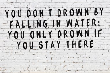 Beyaz tuğla duvara zekice alıntılar yazılı siyah bir yazı.