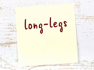 Uzun bacaklarla ilgili bir hatırlatma. Tahta duvarda üzerinde yazı olan sarı yapışkan kağıt.