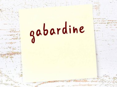 Tahta duvardaki sarı yapışkan notta el yazısıyla yazılmış gabardin yazısı var.