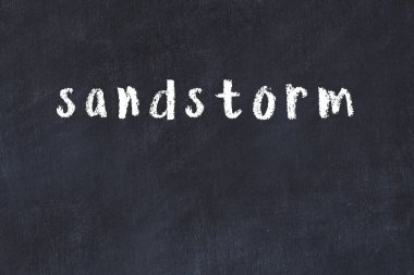 Tebeşir el yazısıyla yazılmış kum fırtınası siyah masanın üzerinde