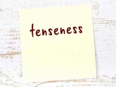 Tahta duvardaki sarı yapışkan notada el yazısıyla yazılmış gerginlik var.