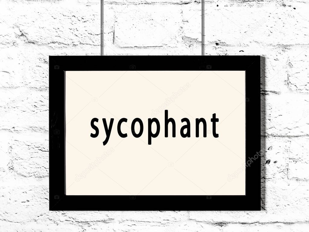 Black wooden frame with inscription sycophant hanging on white brick wall 