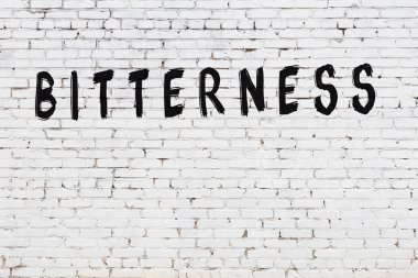 Beyaz tuğlalı duvar, siyah boyayla yazılmış sert yazı.