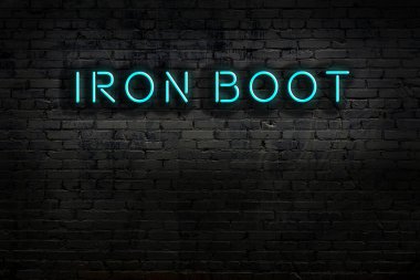 Duvara kazınmış demir çizmeli neon tabela. Gece görünümü