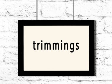 Siyah ahşap çerçeve, beyaz tuğla duvarda yazı süslemeleri asılı. 