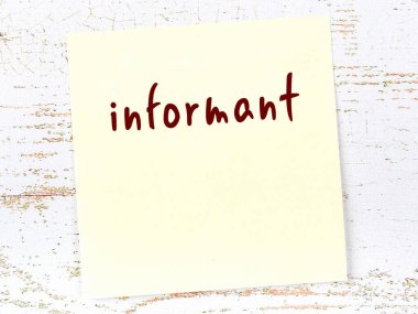 Tahta duvardaki sarı yapışkan notta el yazısıyla yazılmış muhbir var.