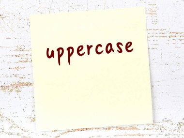 Büyük harfle hatırlatma kavramı. Tahta duvarda üzerinde yazı olan sarı yapışkan kağıt.