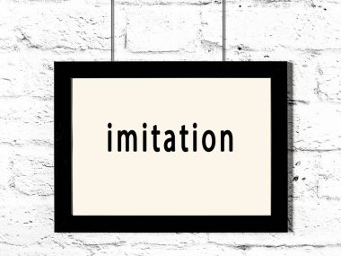 Siyah ahşap çerçeve, beyaz tuğla duvara yazı taklidi asılmış. 