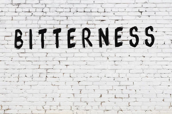 Beyaz tuğlalı duvar, siyah boyayla yazılmış sert yazı.