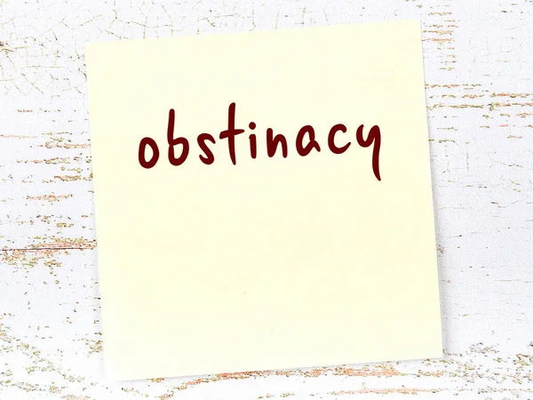 Tahta duvardaki sarı yapışkan notta el yazısıyla yazılmış inatçılık var.