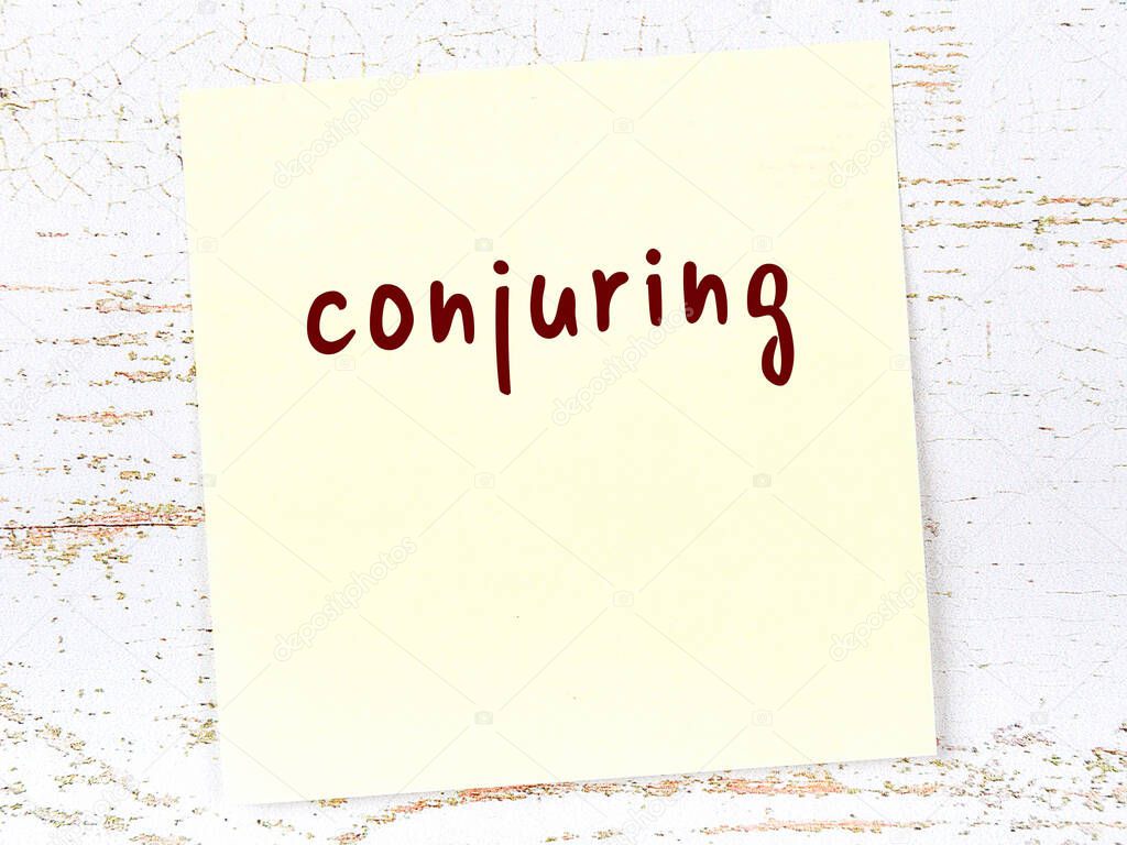 Concept of reminder about conjuring. Yellow sticky sheet of paper on wooden wall with inscription