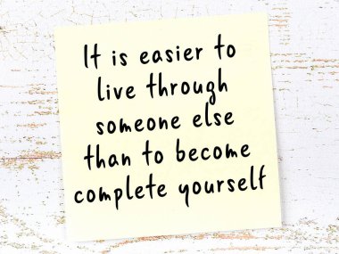 Tahta duvarda asılı sarı yapışkan nota elle yazılmış bilgece bir alıntı.