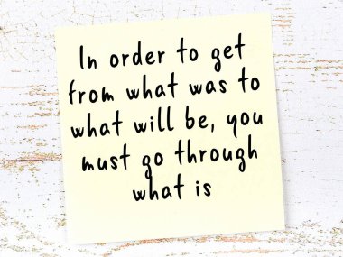 Tahta duvarda asılı sarı yapışkan nota elle yazılmış bilgece bir alıntı.