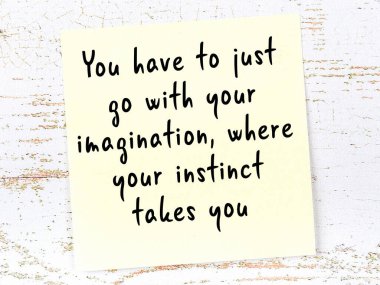 Tahta duvarda asılı sarı yapışkan nota elle yazılmış bilgece bir alıntı.